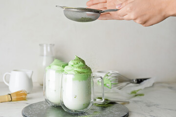 Woman preparing tasty dalgona matcha latte on light background