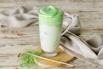 Cup of tasty dalgona matcha latte, powder and chashaku on light wooden background