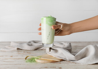 Woman holding cup of tasty dalgona matcha latte on light wooden background