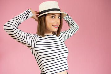 Portrait of young beautiful woman wearing straw hat smiling looking at camera over pink background.