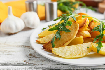 Plate of tasty baked potato with garlic on light wooden background