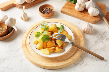 Plate of tasty baked potato with garlic on light background