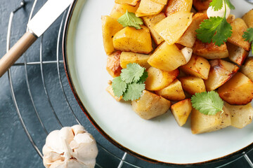 Plate of tasty baked potato with garlic on dark background, closeup