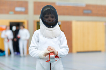 Little kid boy fencing on a fence competition. Child in white fencer uniform with mask and sabre....