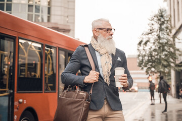 Portrait business man going to work. Serious hipster entrepreneur drinking coffee while waiting bus. Transport and job concept.