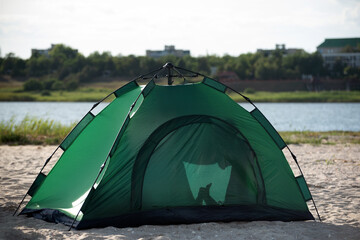 Tourist tent on sandy bank against river background. Camping rest outside the city