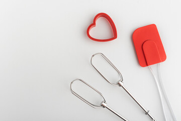 Mixer whisk, kitchen silicone spatula and heart-shaped cookie cutter, white background.