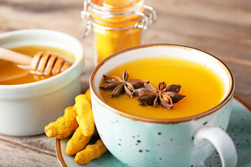 Cup of healthy turmeric drink and honey on wooden background