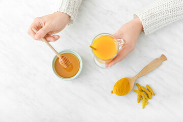 Woman making healthy turmeric drink with honey on light background