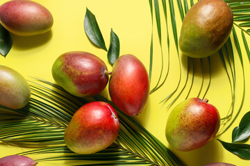 Sweet ripe mangoes and tropical leaf on color background