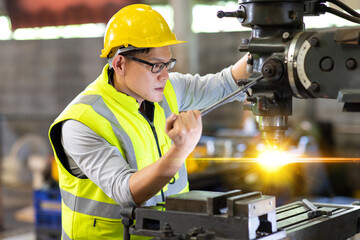 Asian man worker wearing safety hardhat helmet control lathe machine to drill components. Metal lathe industrial manufacturing factory