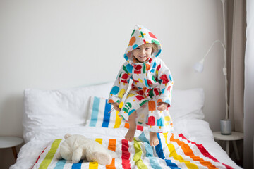 Happy toddler child, blond boy with colorful bathrobe, jumping on the bed