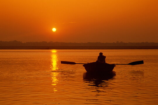 Figure in rowing boat silhouetted at sunset, River Ganges, Varanasi (Benares), Uttar Pradesh state