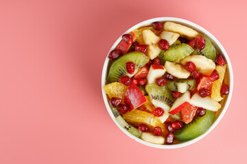Salad of different juicy ripe fruits in a white cup on a pink background.