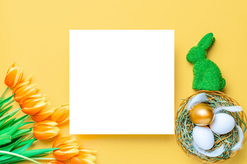 Basket easter decoration: Golden eggs in basket with spring tulips, white feathers on pastel yellow background. Congratulatory easter design. Top view.