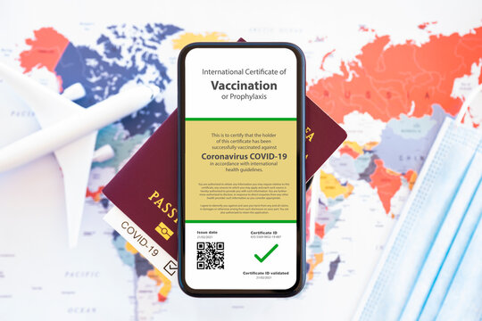 A passport and a smartphone with a certificate of vaccination against the Covid-19 are arranged on a blurred World Map. Travel concept during the Coronavirus pandemic.