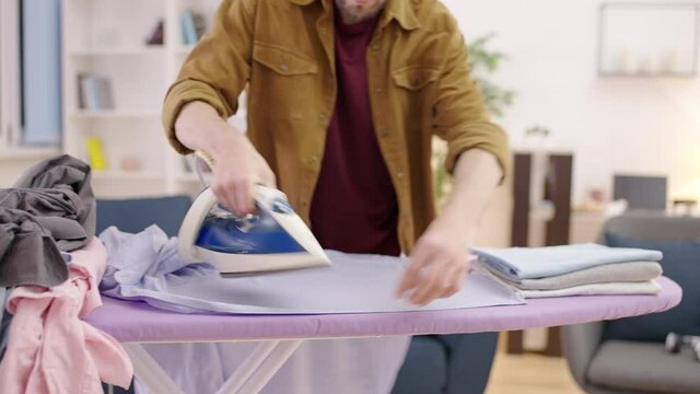 Tidy man ironing shirt at home, diligent husband doing household chores, laundry