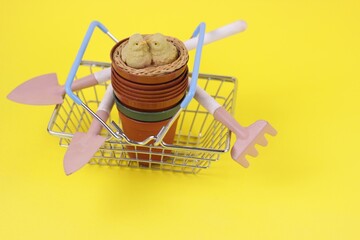 Gardening tools, flowers pots and birds figure in shopping basket on yellow background.Spring Garden Works Concept.