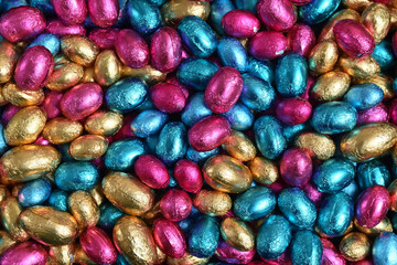 Fototapeta na wymiar Large & small pink, blue and gold foil wrapped chocolate easter eggs, against a peach orange background.