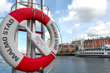 Obraz premium Pole with a lifebuoy at the sea entrance to the city of Malmo Sweden background of ship and buildings of the place