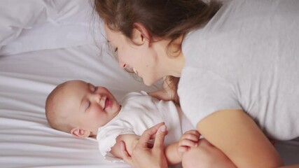 Loving young mommy hugging soothing adorable sweet baby girl lying in bed. Smiling caring mother and cute little infant child girl cuddling in bedroom. Mum and child tender moments.