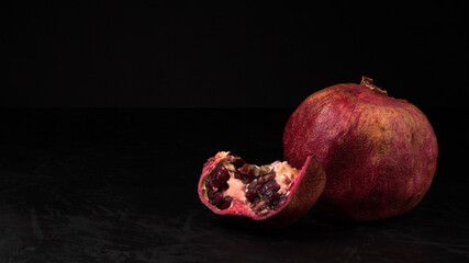 red pomegranate whole and a slice on a black background. dark artistic still life with copy space