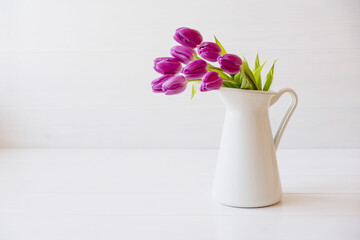 Beautiful mono bouquet of purple tulips in full bloom in white vase on white background. Copy space for text. Spring still life.