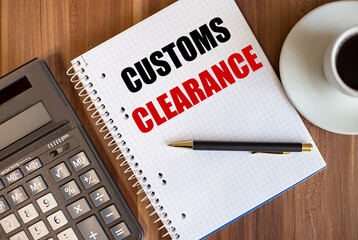 CUSTOMS CLEARANCE written in a white notepad near a calculator and a cup of coffee on a dark wooden background