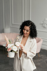 Woman with curly hair in beige suit with a bouquet of flowers