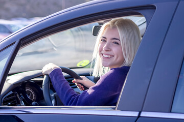 Young smiling woman steering car at sunset