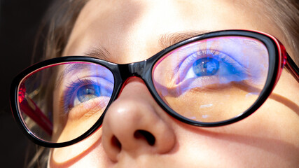 Close up of woman's eyes with red and black female glasses for working at a computer with a blue...
