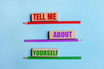 On a blue background, three colored pencils, three wooden blocks with text TELL ME ABOUT YOURSELF
