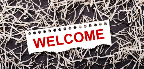 A white sheet of paper with the text WELCOME lies on white shavings on a dark background. © Елена Дигилевич