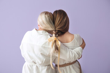 Young woman and her mother with braided together hair on color background, back view