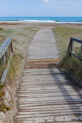 A wooden boardwalk leading through coastal marshlands and sand dunes to the sea beach at San Pedro del Pinatar park, Murcia, Spain