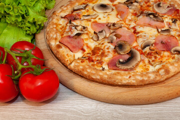 Pizza with ham, mushrooms and cheese on a board with tomatoes and green salad