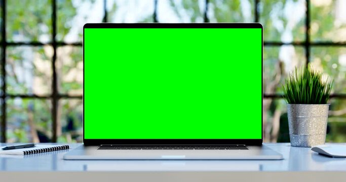 Laptop with blank green screen. Static footage with trees swaying or moving in the wind. Home interior or loft office background, 4k 24fps UHD, loop video