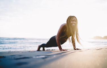 Smiling African American female trainer with casual figure feeling excited while doing push up...