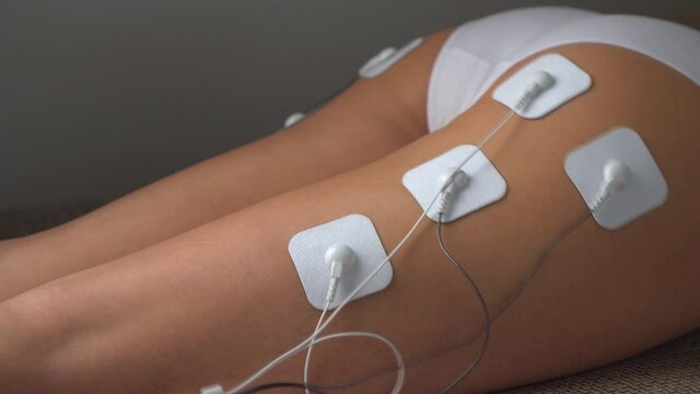 Woman doing electrical stimulation massage on the Buttocks Tens. Myostimulation of the girl's buttocks and legs with vibration impulses from the electrodes