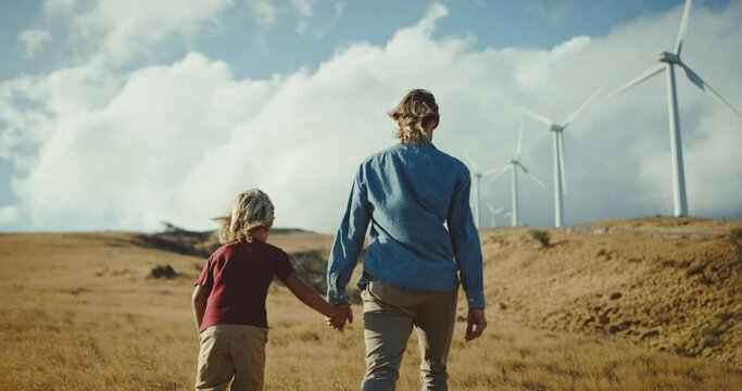 Adventurous father and son hiking up hillside with windmills, family lifestyle, quality time together, clean energy for future generations