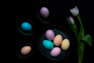 Fototapeta na wymiar Tulip flowers and pastel colored Easter eggs in a dark granite plate against Black background.