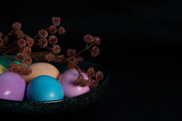 Side view of  flowers and pastel colored Easter eggs in a dark granite plate against Black background.