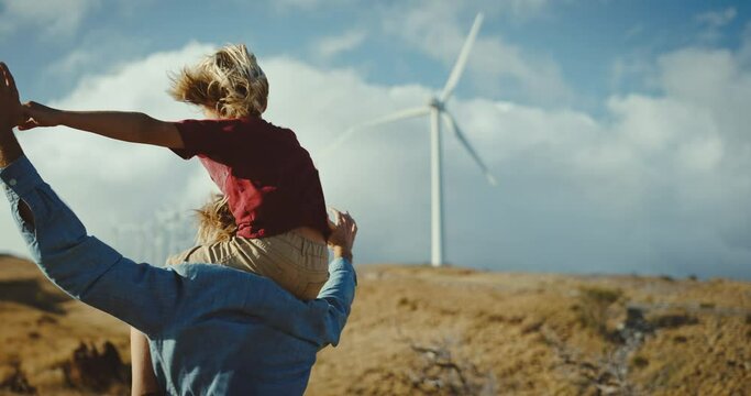 Father and son playing looking out at windmills on golden hillside, dreaming of a clean and sustainable future for generations to come, heart warming uplifting picture of clean energy