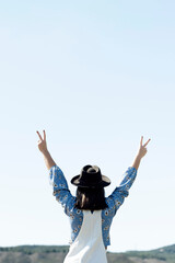 Backside of a victory sign a woman with hat and blue sky background.