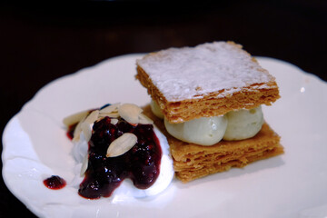 Snack made by baked bread, cream, blueberry, and icing sugar on white plate