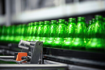 Automated conveyor line in a brewery. Rows of green glass bottles on the conveyor close-up....