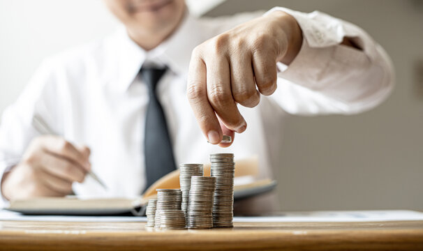 Businessmen are stacking coins on top of the highest row, saving money for growth by taking their monthly savings to fund or invest. Concept of saving money for investment.