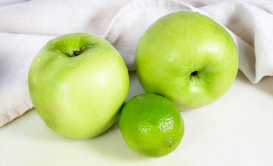 Two green apples and one whole lime on the table. The concept of a green diet.