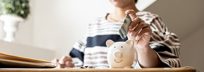 A business woman is putting dollar bills in a white pig piggy bank to save, she is doing an income...