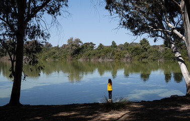 Young girl standing at the edge of a lake looking at duck birds. Children outdoor activities.